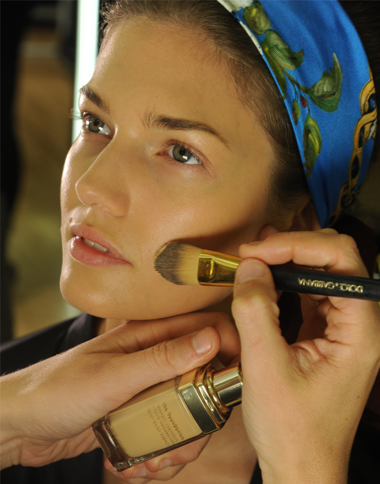 A makeup artist applies foundation to a model backstage at Dolce & Gabbana's Spring/Summer 2013 runway show